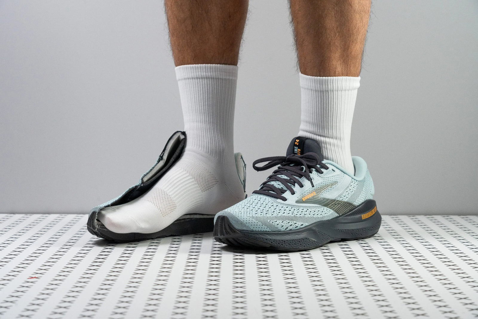 One foot wears a Brooks running shoe; the other shows a cut‑open Brooks shoe revealing its layers.