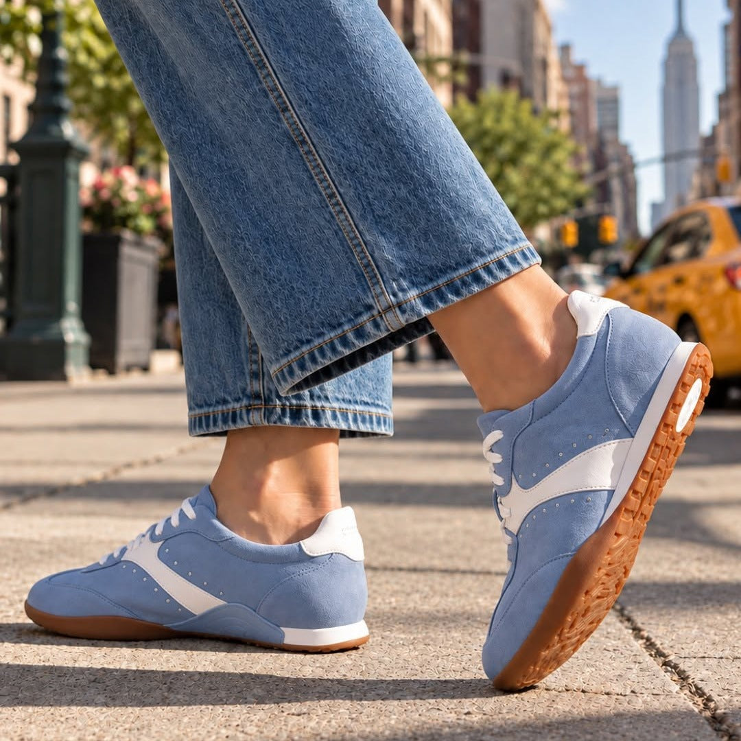 Woman walking on a city sidewalk in light blue suede Aetrex Sloane sneakers with white accents and gum soles