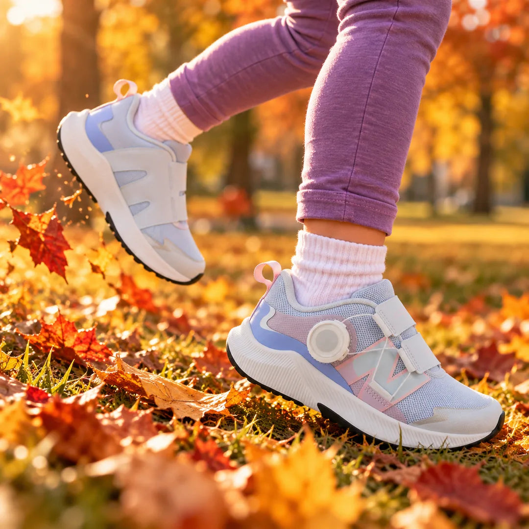 Child running through fall leaves in New Balance DynaSoft Reveal V4 BOA kids' running shoes in Ice Blue and Rose Sugar