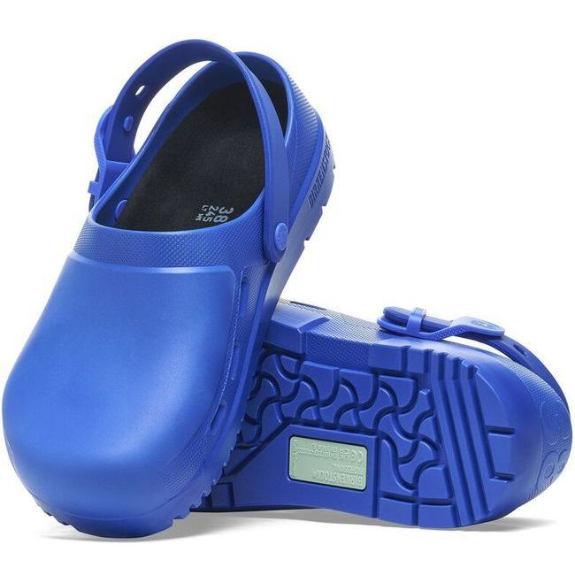 View of a pair of blue Birkenstock Unisex Birki Air 2.0 Professional Clogs, with one shoe displaying the oil- and grease-resistant polyurethane sole while the other shoe leans against it to show the top view. The top highlights the fluid-resistant design ideal for healthcare and utility, featuring side air vents for breathability and adjustable, detergent-friendly backstraps for a secure fit.