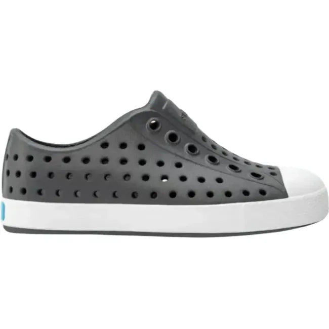 Lateral side view of the Native Kids' Jefferson Shoe in dark gray, featuring a slip-on design, lightweight and hand-washable Sugarlite™ material, a perforated upper similar to Crocs, and a white toe cap for added design.