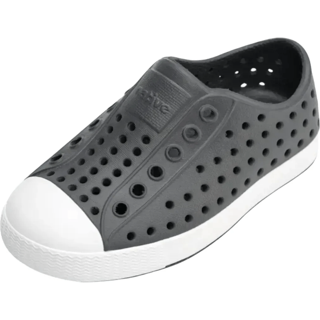 Overhead view of the Native Kids' Jefferson Shoe in dark gray, featuring a slip-on design, lightweight and hand-washable Sugarlite™ material, a perforated upper similar to Crocs, a white toe cap, and a white sole.
