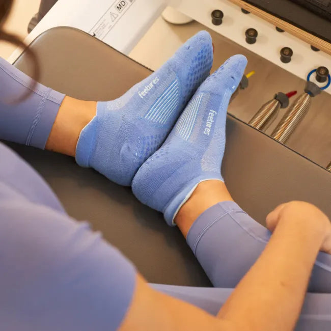 Woman wearing Feetures Elite Grip Max Cushion Tab Socks in Flex Blue, shown on Pilates reformer