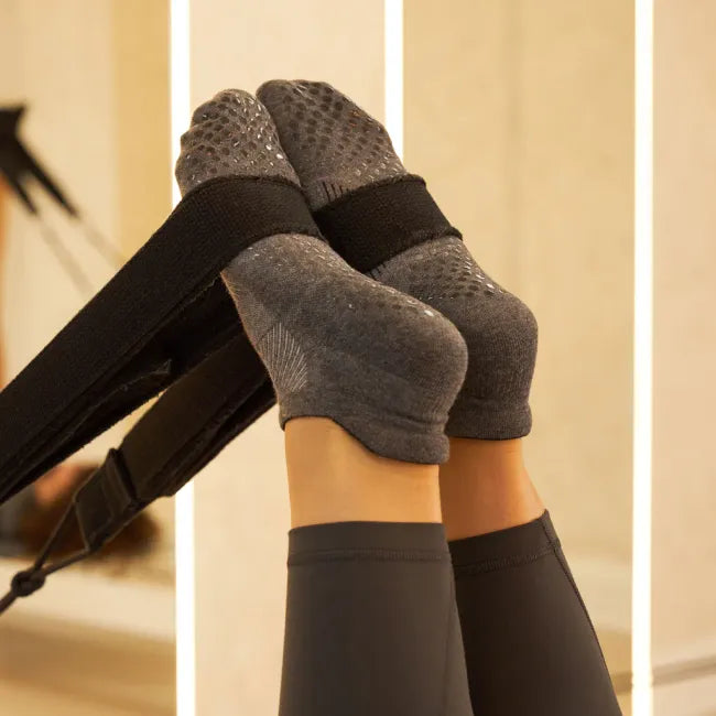 Feet in Women's Feetures Elite Grip Sock in Flow Gray, shown in Pilates reformer straps; grip soles