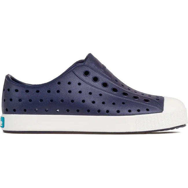 Lateral side view of the Native Kids' Jefferson Shoe in navy blue, featuring a slip-on design, lightweight and hand-washable Sugarlite™ material, a perforated upper similar to Crocs, and a white toe cap for added design.