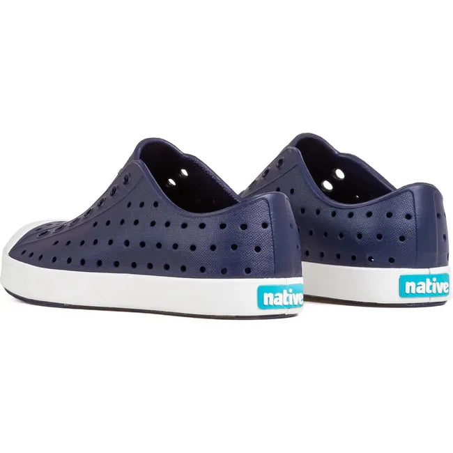 Heel view of a pair of Native Kids' Jefferson Shoes in navy blue, featuring perforated uppers similar to Crocs, white soles, and 'Native' branding in blue around the heels.