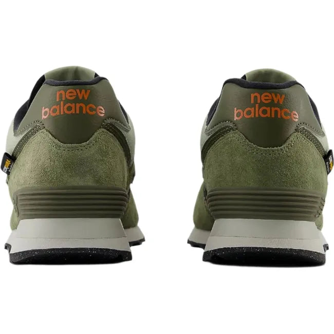 Heels of Unisex New Balance 574 sneakers in olive green suede with orange accents.